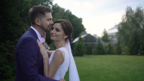 Portrait latéral sensible du couple adorable de jeunes mariés dans l'amour serrant tendrement dans le jardin . — Video