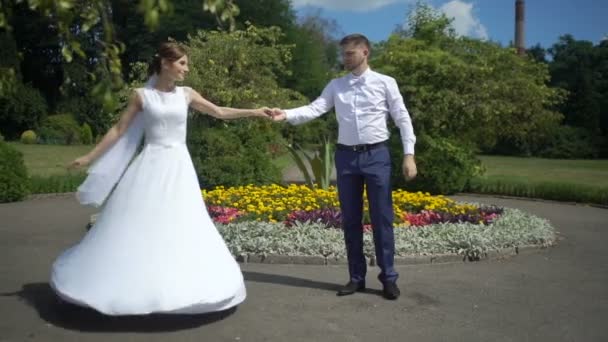 Incríveis recém-casados em roupas elegantes estão sorrindo e dançando no jardim ensolarado florescendo . — Vídeo de Stock