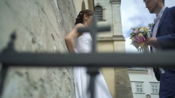 Stilig snygga brudgummen i blå kostym och bröllop bukett av färgglada rosor kommer till sin charmiga brud med vackra leende och kysser henne. — Stockvideo