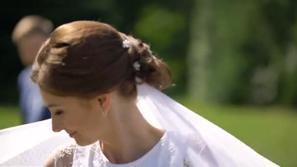 Очаровательная невеста с темными волосами и красивой улыбкой крутится и играет со своей идеальной белой вуалью . — стоковое видео