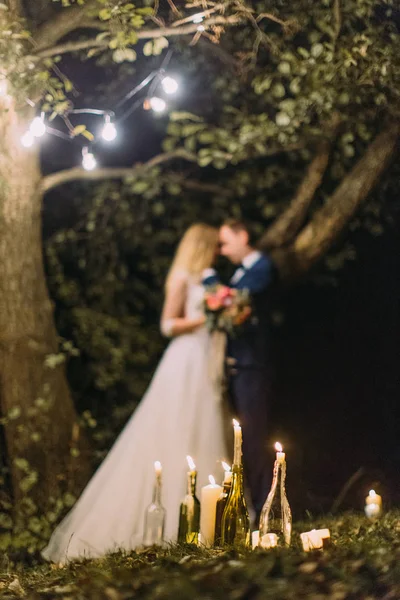 The composition of the candles in glass bottles at the background of the hugging newlyweds. — Stock Photo, Image