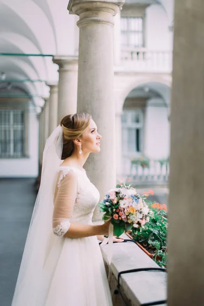 Боковой портрет красивой невесты, держащей свадебный букет, стоя на старом балконе . — стоковое фото