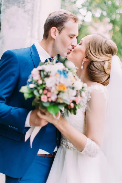 Vue latérale du baiser jeunes mariés tenant le bouquet de mariage . — Photo