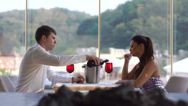 Hermosa pareja joven en la fecha en el restaurante de lujo. El hombre elegante está vertiendo vino tinto en vasos . — Vídeo de stock