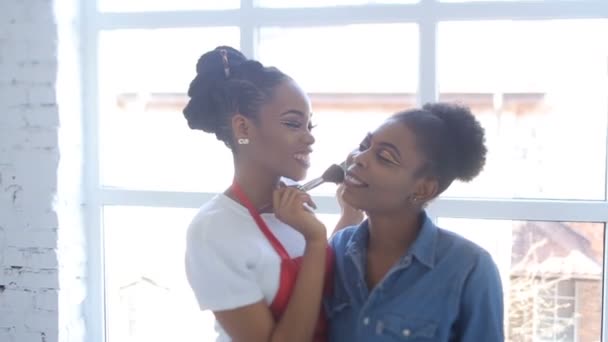 Sorrindo afro-americano make-up artista está aplicando o pó na face do modelo africano. Branco estúdio localização . — Vídeo de Stock