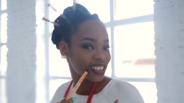 Adorable artista de maquillaje profesional africano está posando con el conjunto de pinceles en el estudio blanco . — Vídeos de Stock