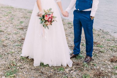 Sahilde duran yeni evliler bacaklar görünümü. Mükemmel bir düğün buket görünümünü.