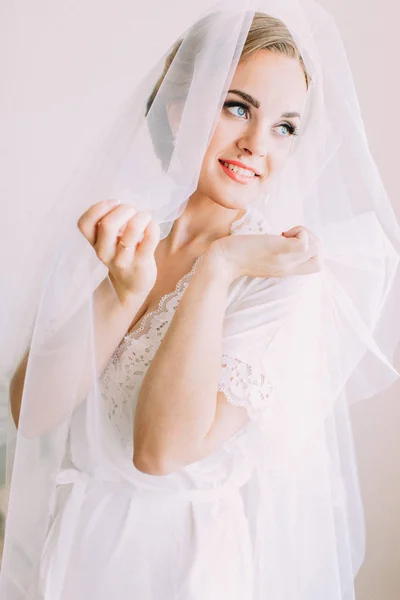 Half-length portrait of the smiling bride covered with wedding veil looking aside.