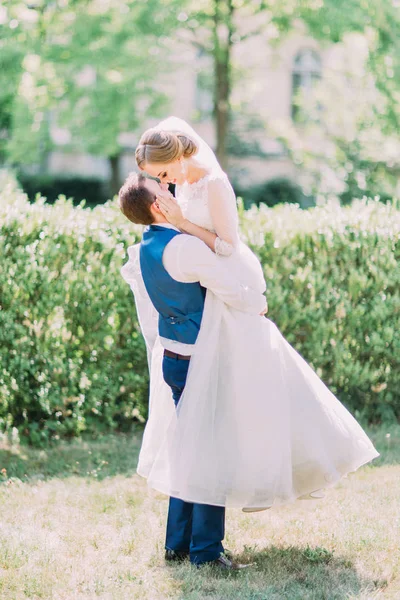 The handsome groom is carrying the bride while she is stroking his cheek. — Stock Photo, Image