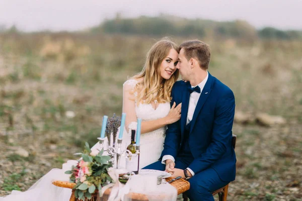 De horizontale weergave van de close-up van de knuffelen pasgetrouwden zitten aan de tafel van de bruiloft aan de kust. — Stockfoto