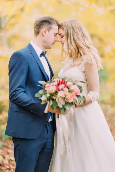 Retrato de medio cuerpo de los recién casados de pie cabeza a cabeza con el ramo de bodas . —  Fotos de Stock