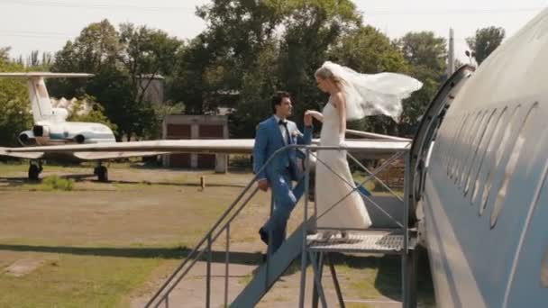 Vue pleine longueur au charmant couple heureux nouvellement marié embrassant tendrement près de l'avion . — Video