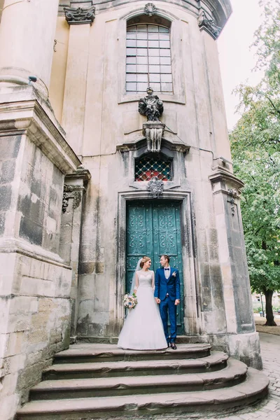 Vista completa de los recién casados felices tomados de la mano mientras están de pie cerca del antiguo edificio . —  Fotos de Stock