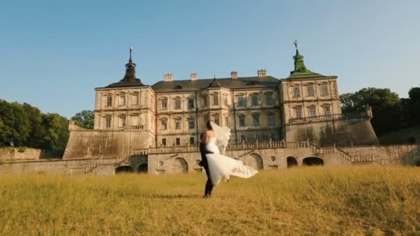 Schöner Bräutigam hebt ab und dreht sich um seine wunderschöne Braut im Hintergrund des alten Palastes während des Sonnenuntergangs. — Stockvideo