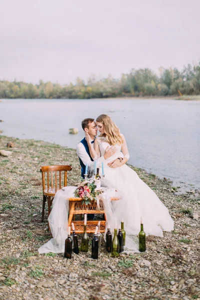 Nevěsta sedí na kolenou ženicha na svatební tabuli umístěné na pláži. — Stock fotografie