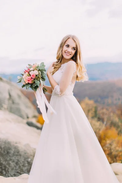 Maravilhosa noiva sorridente com o buquê de casamento está olhando para o lado . — Fotografia de Stock