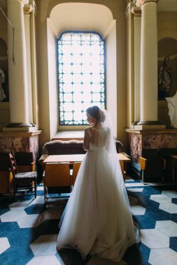 Kilisenin penceresinde yakınındaki şık gelin arkadan görünüm.