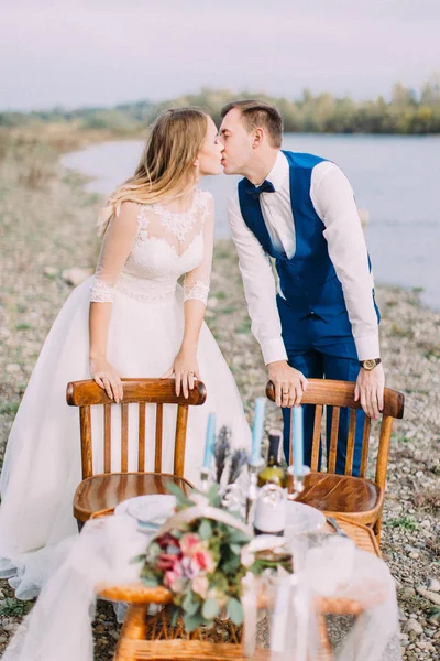 Besar a los recién casados mientras se apoya en las sillas colocadas en la costa . —  Fotos de Stock