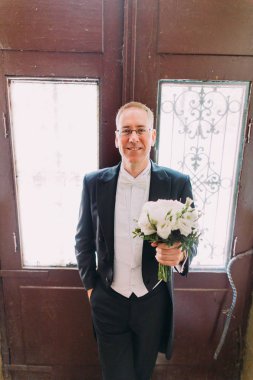 Düğün buketi eski kapının yanında neşeli yakışıklı damat varoluş portresi.