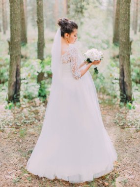 Arkadan görünüşü peonies buket tutarak uzun gelinlik güzel gelin. Orman konumu.