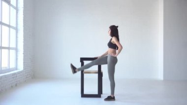 Tam uzunlukta görünümü. Esmer eğitmen tekmeler sandalye beyaz izole Studio yardımıyla yapıyor. 4k.