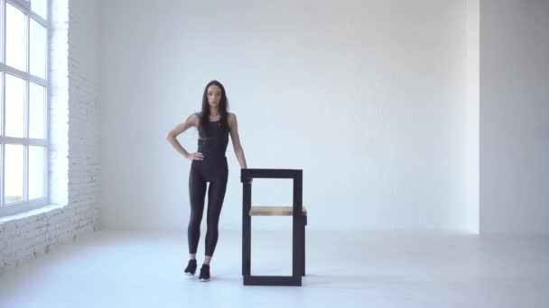 スポーツ ウエアで運動の女性ホワイト スタジオの椅子の助けを借りてサイド キックの実行です。4 k 映像. — ストック動画