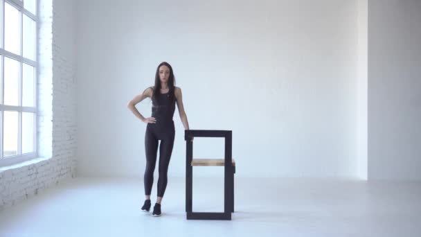 La mujer atlética en ropa deportiva está realizando patadas laterales con la ayuda de la silla en el estudio blanco. Imágenes de 4k . — Vídeos de Stock