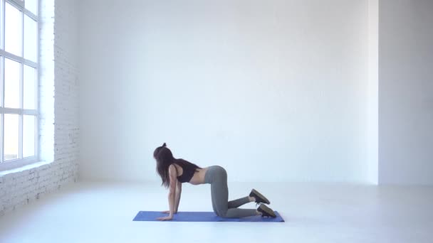 De magere atletische vrouw in het doen van de oefening ezel-kick op de mat van de yoga in witte studio. 4 k-beeldmateriaal. — Stockvideo