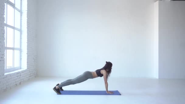 Full-length view of the young sportive trainer standing in plank pose and raising hands up in the white isolated studio. 4k. — Stock Video