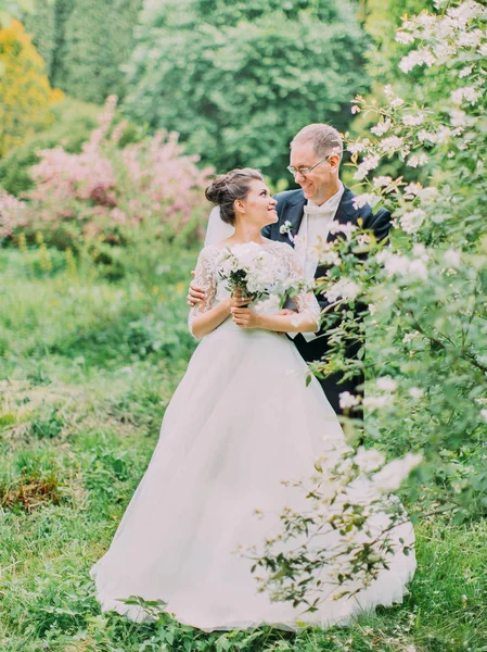 Foto de larga duración de los recién casados abrazos felices caminando en el jardín verde . —  Fotos de Stock