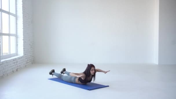 Mulher fitness saudável está esticando as costas. Ela está fazendo de volta extensões no tapete de exercícios em estúdio branco. 4k . — Vídeo de Stock