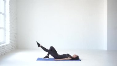 Sağlıklı sportif kadın egzersiz mindere yalan ve beyaz Studio bacağını yukarı kaldırma tam uzunlukta görünümünü. 4k.