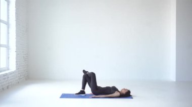 Isınma egzersizleri. Çekici sportif kadın mindere diz ve kaldırma uo bacak ile onu geri yalan söylüyor. 4 k görüntüleri.