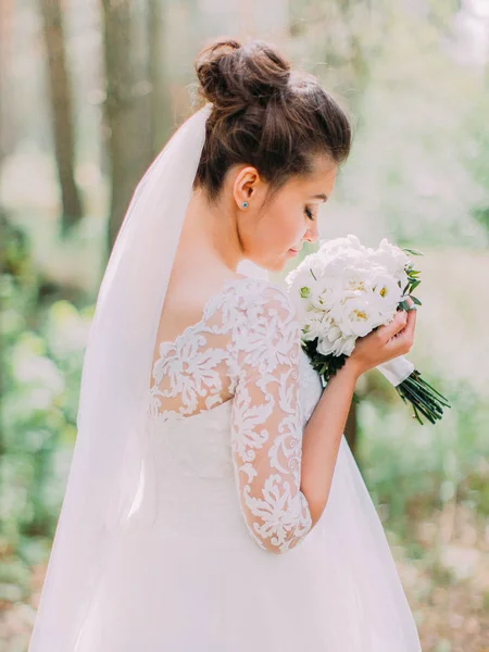 A noiva encantadora está cheirando o buquê de casamento de peônias brancas. A vista traseira . — Fotografia de Stock