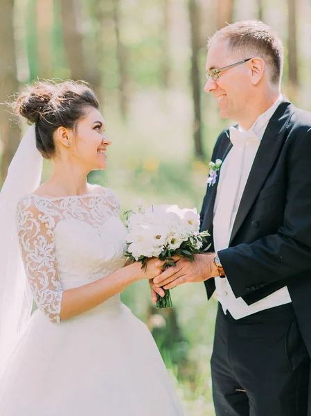 Yan görünüm beyaz peonies düğün buket holding neşeli yeni evliler. Orman konumu.