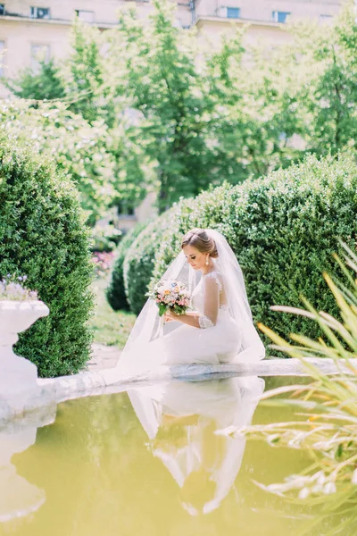 Прекрасная невеста сидит на фонтане. Вид сбоку . — стоковое фото