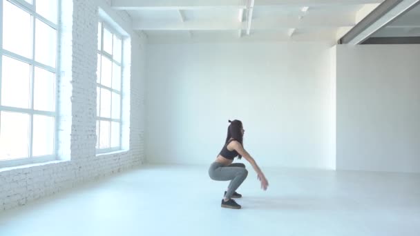 Vue latérale complète de la sportive qui fait des squats et lève les mains. Emplacement du studio . — Video