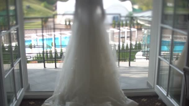 Rückansicht der stylischen blonden Braut im wunderschönen weißen und langen Brautkleid, die auf der Terrasse spaziert.