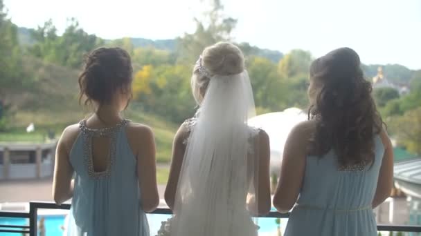 Vista trasera de la novia perfecta y sus dos damas de honor en vestidos azules de pie en el balcón, girando, saludando la mano y girando hacia atrás . — Vídeos de Stock