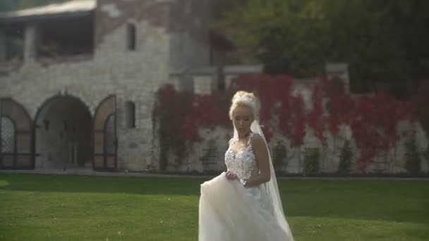 Teljes nézet th vonzó szőke menyasszony fut végig a kertben, a naplemente alatt hosszú elegáns esküvői ruha.