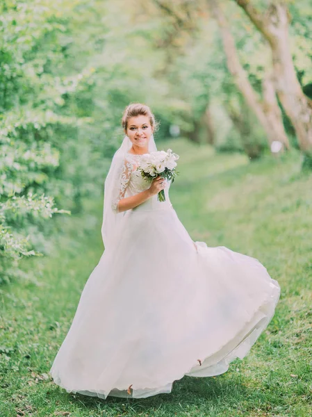 Gelinlikle yeşil orman ile oynarken gülümseyen gelinin tam uzunlukta görünümü.