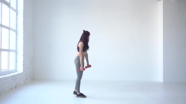 Full-length zijaanzicht van de magere Sportvrouw doen de squats met dumbbels. Ze is het verhogen van been omhoog terwijl het neerlaten van terug. 4k. — Stockvideo