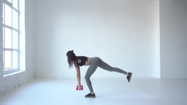Kardio cvičení. Sportovní dívka dělá dřepy s činkami a pozvedá nohy v bílých studio. 4 k video. — Stock video