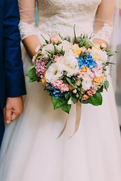 Th vista vertical close-up do buquê de casamento de flores brancas, azuis e rosa nas mãos da noiva . — Fotografia de Stock