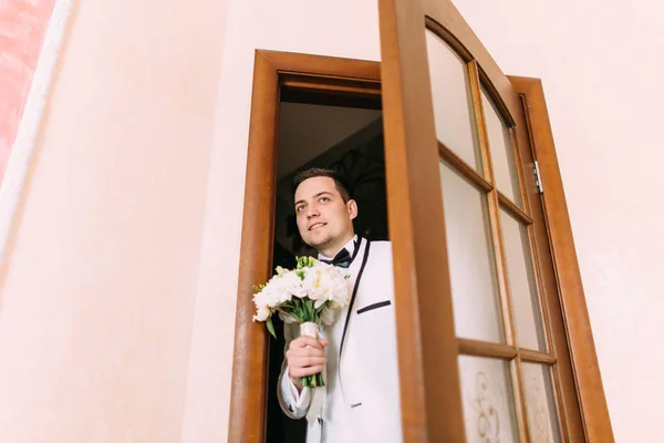 Ο γαμπρός με τη γαμήλια ανθοδέσμη από τριαντάφυλλα ανοίγει την πόρτα. — Φωτογραφία Αρχείου