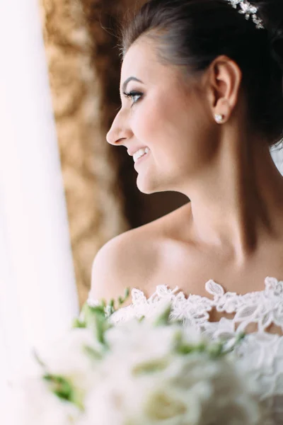 Vista lateral close-up da noiva sorridente com buquê de casamento olhando pela janela . — Fotografia de Stock