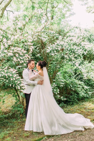 Heureux jeunes mariés passant du temps dans le jardin. La mariée caresse le visage du marié . — Photo