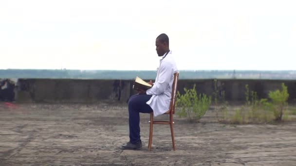 Confident african psychotherapist is resting with the book on the roof of the old ruined hospital. — Stock Video