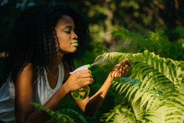 Gorgeours genç çekici Afrika kızla yeşil göz gölgeler ve yeşil plastik tetikleyici kullanma ferns püskürtme ruj. Yeşil kavram. Açık.