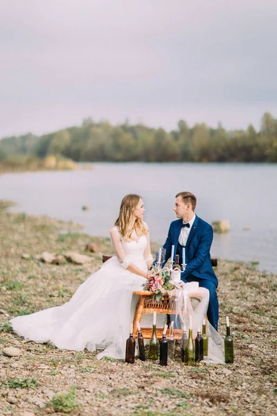 Ολόσωμο θέα στο νεόνυμφο ζευγάρι που κάθεται στο τραπέζι γάμου υπέροχο wedcorated στην ακτή. — Φωτογραφία Αρχείου